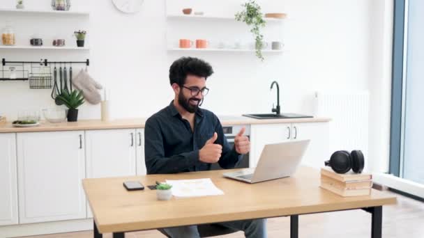 自宅で仕事をしながらコンピュータの前で親指を上げるジェスチャーを示すビジネスヘッドセットの陽気な大人 ビデオ通話アプリを介してプロジェクト戦略の承認を表す効率的なフリーランスの労働者 — ストック動画