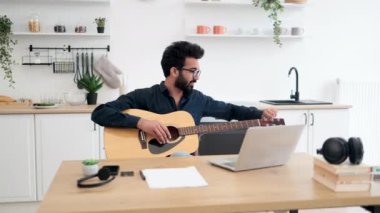 Geniş apartmandaki taşınabilir bilgisayar webcam 'ine gülümserken telli çalgılar tutan neşeli bir Arap. Mutlu gözlüklü erkek modern teknolojileri kullanarak online gitar dersi veriyor..