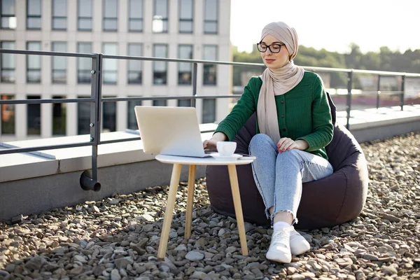 Приваблива Мусульманка Хустці Працює Сучасним Ноутбуком Кавовому Столі Приймаючи Сидіння — стокове фото