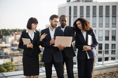 Uzaktan kumandalı bilgisayarı elinde tutan ve mali araştırmaların detaylarını iş ortaklarıyla paylaşan beyaz girişimci. Yan yana duran ve ekrana bakan dört çok ırklı meslektaşım..