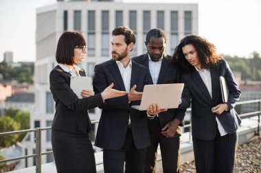 Bilgisayar monitörüne bakan ve yeni iş projesiyle ilgili yeni fikirleri paylaşan dört proaktif şirket ortağı. Kişisel aletleri olan çok ırklı iş arkadaşları çatıda toplanıyor..