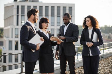 Bir grup uluslararası şirket yatırımcısı şirket çatısında toplanırken işbirliği anlaşması imzalıyor. Afrikalı Amerikalı işadamı dijital tablete elektronik imza atıyor.