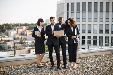 Terasta taşınabilir aletlerle ayakta duran ve pazarlama stratejilerini tartışan çok kültürlü finansörler. Zarif takım elbiseli iş arkadaşları ekranda izliyor ve önemli konular hakkında tartışıyorlar.