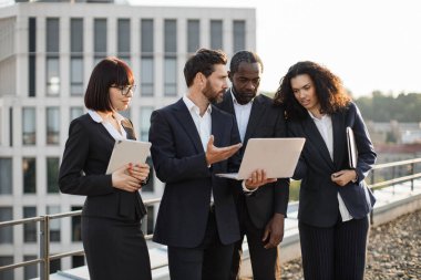 Bilgisayar monitörüne bakan ve yeni iş projesiyle ilgili yeni fikirleri paylaşan dört proaktif şirket ortağı. Kişisel aletleri olan çok ırklı iş arkadaşları çatıda toplanıyor..