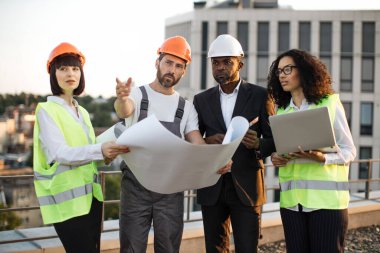 Çok ırklı endüstriyel çalışanlardan oluşan bir grup panoramik terasta proje inşa etmeyi ve buluşmayı planlıyor. İş merkezinin yenilenmesi için bilgisayar ve teknik plan kullanan dört uluslararası meslektaşım.