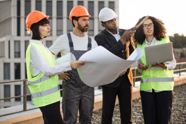 Çok ırklı endüstriyel çalışanlardan oluşan bir grup panoramik terasta proje inşa etmeyi ve buluşmayı planlıyor. İş merkezinin yenilenmesi için bilgisayar ve teknik plan kullanan dört uluslararası meslektaşım.