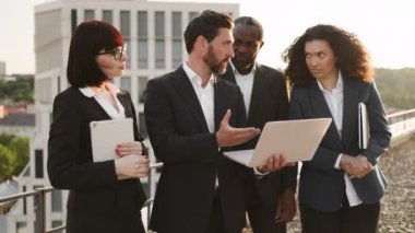 Bilgisayar monitörüne bakan ve yeni iş projesiyle ilgili yeni fikirleri paylaşan dört proaktif şirket ortağı. Kişisel aletleri olan çok ırklı iş arkadaşları çatıda toplanıyor..