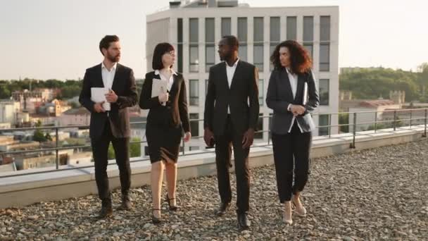 成功した合意をした後に誇らしげに歩くスーツを着た異なる民族のビジネス投資家のチーム 男性と女性の専門家がコンテンツを感じ オフィスの屋上を離れる — ストック動画