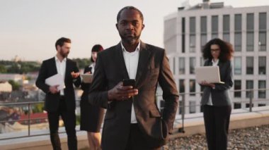 Elinde cep telefonu tutan ve kameraya gülümseyen başarılı Afrikalı Amerikalı girişimcinin portresi. Proje yönetimi için kişisel araçlar kullanan karışık uyruklu iş ortakları.