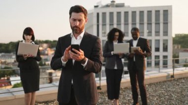 İş ortakları arka planda taşınabilir cihazlar kullanırken beyaz sakallı girişimci akıllı telefondan numara çeviriyor. Çok ırklı yatırımcılar yeni bir kompleks oluşturma planı üzerinde birlikte çalışıyorlar.