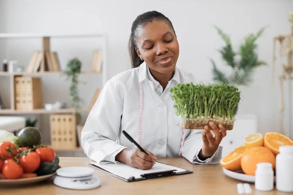 若い芽を手にした積極的な女性栄養士は 医師事務所で食事食事を作成します アフリカ系アメリカ人の専門家を測定テープをお勧めします顧客痩身食品 — ストック写真