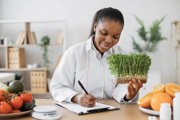 若い芽を手にした積極的な女性栄養士は 医師事務所で食事食事を作成します アフリカ系アメリカ人の専門家を測定テープをお勧めします顧客痩身食品 — ストック写真