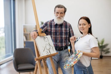 Neşeli son sınıf beyefendisi ve genç bayan sehpanın yanında tuvalde erkek portresi ile poz veriyorlar. Becerikli amatör ressam atölyedeki resim çalışmasında kafa ve omuz çizimini tamamlıyor..