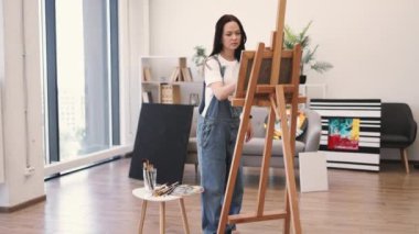 Beyaz tenli çekici bir kadın tuvale fırça darbeleri uyguluyor. İçerideki ahşap sehpa ile destekleniyor. Serbest çalışan ressam, resim stüdyosunun rahatlığını kullanarak ışık ve gölge oyunlarına konsantre oluyor..