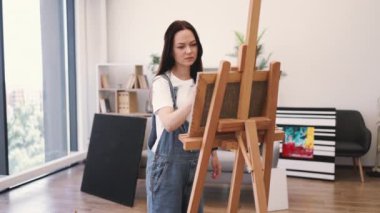 Beyaz tenli çekici bir kadın tuvale fırça darbeleri uyguluyor. İçerideki ahşap sehpa ile destekleniyor. Serbest çalışan ressam, resim stüdyosunun rahatlığını kullanarak ışık ve gölge oyunlarına konsantre oluyor..