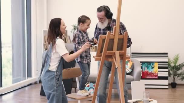 Joven Mujer Descalza Con Auriculares Móvil Mirando Niña Aplicando Pintura — Vídeos de Stock