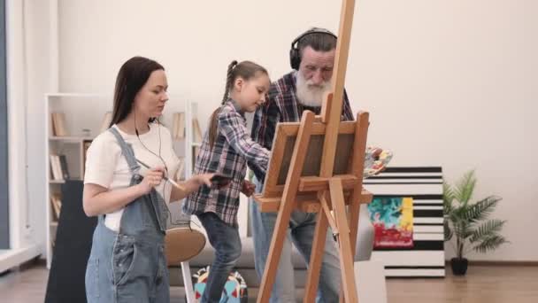 Wanita Santai Dengan Earbuds Membuat Kolase Atas Kanvas Dengan Anak — Stok Video
