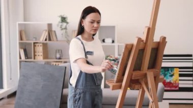 Beyaz tenli çekici bir kadın tuvale fırça darbeleri uyguluyor. İçerideki ahşap sehpa ile destekleniyor. Serbest çalışan ressam, resim stüdyosunun rahatlığını kullanarak ışık ve gölge oyunlarına konsantre oluyor..