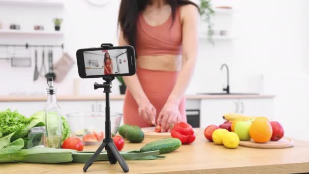 ブルネットの女性スライストマトのカッティングボードのクロップビューとモバイルでのプロセスの記録を得る アクティブウェアのアスレチック成人 栄養豊富な野菜を介して食事の変更についてブログ — ストック動画