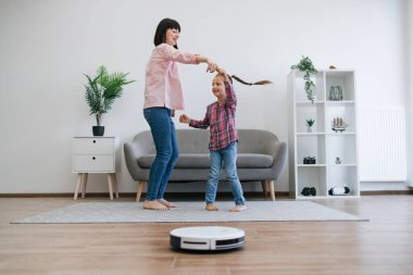 Neşeli anne, küçük çocuğu enerjik melodilere yönlendirirken robot temizleyicisi de evdeki pislikle uğraşıyor. Mutlu aile hanımları ev işlerini ev içi aktivitelere dönüştürüyor..