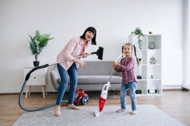 Heyecanlı kadın ve mutlu kız, müzik ekipmanları yerine elektrikli süpürgelerle sahte ev konseri veriyor. Duygusal ebeveyn ve yetenekli çocuk ev işleri yaparken değerli anlar yaratıyor..