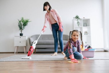 Süpürgeyle halıdaki tozu temizlerken, lastik eldivenli reşit olmayan bir çocuk toprağı temizliyor. Yorulmak bilmeyen ev hanımları ev işleriyle ilgilenerek alerji riskini azaltıyor..