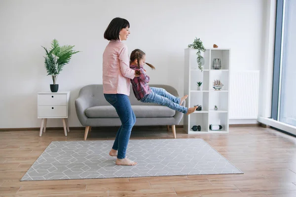 Modern salonda küçük bir kızı döndürürken çocuğu koltukaltı altında tutan gündelik kıyafetlerle aktif bir kadın. Şefkatli anne evdeki tatlı kızına sıfır yerçekimi uçuşu eğlencesi sunuyor..