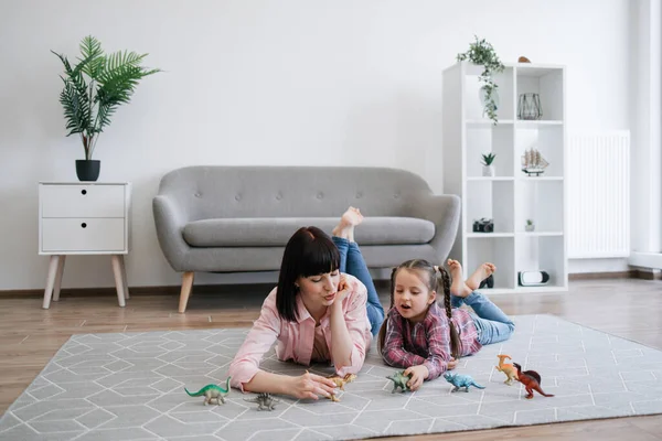Playful tween girl with animal toy having fun with brunette woman in living room of spacious apartment. Mindful mother encouraging scientific exploration while keeping daughter entertained indoors.