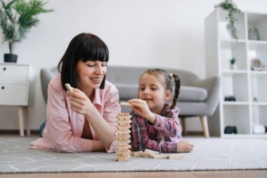 Elinde tahta tuğlayla gülümseyen aile kadını sıcak oturma odasında ergen bir kızla strateji oyunu oynuyor. Neşeli anne ve kız, oyuncak gökdelen yaratırken karar verme becerilerini geliştiriyorlar..