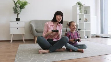 Heyecanlı genç bir kadın ve evde elinde video oyun kontrolörleriyle yerde bacak bacak bacak üstüne atmış küçük bir kız. Aile gündüz vakti sanal dünyada yarışan tutkulu rakipler..