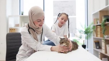 Türbanlı güzel Müslüman veteriner portresi ve modern veteriner kliniğinde sevimli kedisi olan değerli okul çocuğu. Küçük kız evcil hayvanını sağlık kontrolü için getiriyor..