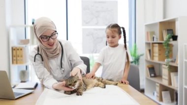 Etkili Müslüman veteriner kürklü hastanın dış kulağını incelerken beyaz bir sahibi masanın yanında duruyor. Başörtüsü takmış bir doktor, hastanede düzenli check-up yaptırırken şişlik arıyor..