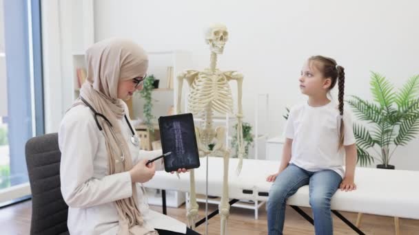 タブレットをスクリーンにCtスキャンしたアラビア人女性の肖像画 デジタルデバイスと解剖モデルを介して脊髄を表すヒジャブの効率的な医師 — ストック動画