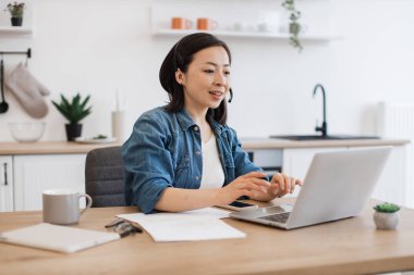 Kot elbiseli Koreli iş kadını beyaz mutfak konforunda bilgisayar aracılığıyla brifinge katılıyor. İnternet uygulaması üzerinden iş arkadaşlarıyla şirket meselelerini tartışmak heyecan verici.