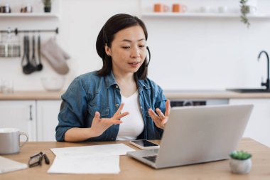 Genç Vietnamlı yetişkin, evdeki taşınabilir cihazlarla grup video konferansı sırasında iş arkadaşıyla sohbet ediyor. Çevrimiçi personel toplantısında iş değişiklikleri konusunda uzman.