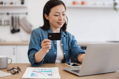 Kısa saçlı güzel Asyalı bir kadın kredi kartı tutuyor ve kişisel bilgisayarına veri giriyordu. Hafif apartmandaki finansal grafiklerle ilgili çevrimiçi işlere girişen ilgili bir kadın..