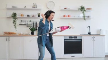 Asyalı çekici bir kadın kablosuz kulaklıkla müzik dinliyor ve elektrikli süpürgeyi gitar gibi tutuyor. Enerjik bir kadın onu rock grubunun bir üyesi gibi hayal ediyor. Eğlence ve ev işleri kavramı.