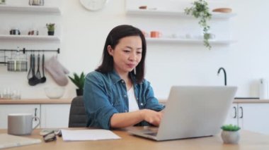 Rahat giyimli barışçıl Vietnamlı kadın modern mutfağın yaratıcı iç mekanında kablosuz teknolojiler kullanıyor. Rahat iş kadını, şirket e-posta hesabını içerideki taşınabilir bilgisayarla kontrol ediyor..