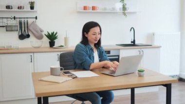 Neşeli Asyalı kadın modern laptopta iyi haberler okurken olumlu duygularını ifade ediyor. Evde mutlu mesut dolaşan, gündelik kıyafetli, pozitif genç bir kadın..