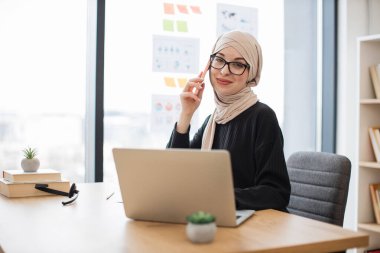 Geleneksel Müslüman başörtülü neşeli bayan dijital ekrandan haberleri okurken akıllı telefondan konuşuyor. Deneyimli çalışanlar iş yerlerindeki şirket verimliliğini artırma fikrini ortaya attılar..