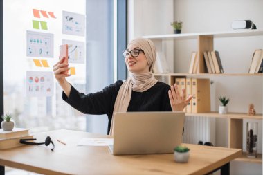Yaratıcı iş yerinde internet uygulaması üzerinden internet üzerinden iletişim kuran neşeli Arap kadın. İş arkadaşlarıyla telefon yoluyla araştırma planı hakkında fikir alışverişinde bulunan heyecanlı bir profesyonel..