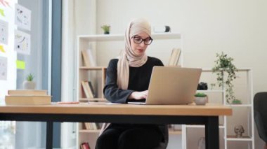 İş yerinde taşınabilir bilgisayar kullanarak etkileşimli grup toplantısına ev sahipliği yapan tesettürlü güzel bir Arap kadın. Verimli baş yönetici bölge ofislerinden pazarlama ekipleriyle konuları tartışıyor..