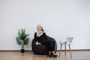 Başörtüsü takmış neşeli Müslüman bir kadın ve cep telefonuyla konuşan, puf minder giymiş. Fotokopi alanı ile işyeri rahatlığında iş konuşmalarını yürüten etkili girişimci.