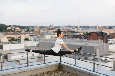 Aktif giyimli güzel, ince bir kadın yaz akşamları çatı korkuluklarının köşesinde ön bölmede çalışıyor. Spor merkezi dışında egzersiz yaparken ortak sağlık ve dengeyi geliştiren atletik genç kadın.