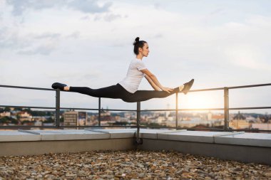 Aktif giyimli güzel, ince bir kadın yaz akşamları çatı korkuluklarının köşesinde ön bölmede çalışıyor. Spor merkezi dışında egzersiz yaparken ortak sağlık ve dengeyi geliştiren atletik genç kadın.