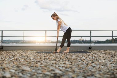Spor salonunun duvarları dışında egzersiz yaparken streç bant kullanan, aktif giyimli beyaz bir kadın. Odaklanmış pratisyen dışarıda direnişe karşı çalışırken çekirdek kaslarını aktif tutuyor..