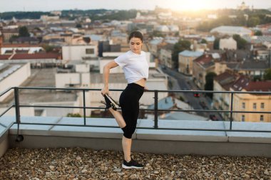 Panoramik terasta egzersiz yapmadan önce spor elbiseli, bacakları ısınan kadın manzarası. Açık hava eğitiminden önce kaslardaki esnekliği arttıran aktif beyaz kadın..