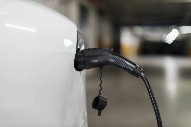Otoparkın otoparkındaki liman üzerinden yükleme kablosuna bağlı elektronik arabanın arka kısmının görüntüsü. Çevre dostu araç halka açık otoparkta elektrikle çalışıyor..