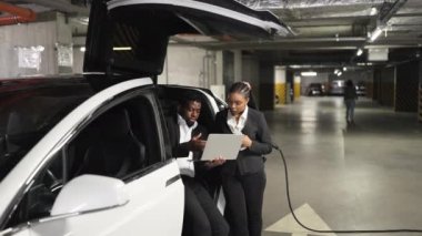 EV 'nin içinde kadın meslektaşı otomotiv yakınlarında otururken Afrika kökenli Amerikalı bir erkeğin bilgisayarı düşük açılı görüntüsü. İş ortakları, bodrumdaki şirket projelerinin video kayıtlarını analiz ediyor..
