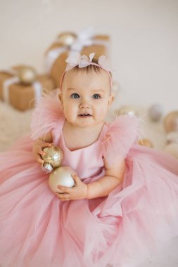 Festivale uygun giyinmiş küçük güzel prenses süslemeli stüdyoda elinde beyaz topla oturuyor. Güzel saç bandı takmış çekici bir bebek. Bakıyor ve doğum günü partisinin tadını çıkarıyor..